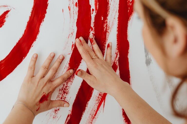 Mains posées sur une toile couverte de traits de peinture rouge, geste libre en art-thérapie