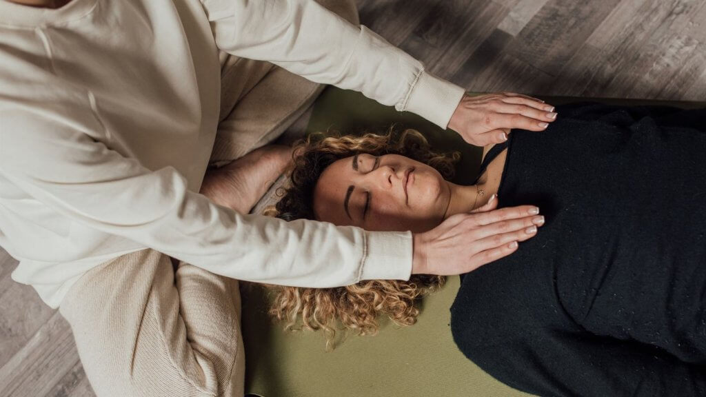 Praticienne posant les mains au-dessus d'une femme allongée, les yeux fermés, pendant un soin énergétique