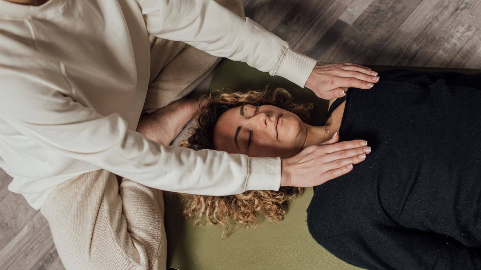 Praticienne posant les mains au-dessus d'une femme allongée, les yeux fermés, pendant un soin énergétique