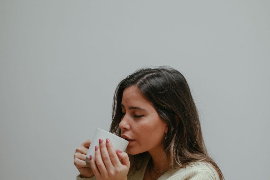 Femme les yeux fermés buvant une boisson chaude, enveloppée dans un plaid