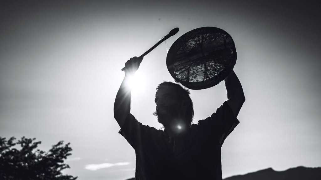 Silhouette d’une personne levant un tambour chamanique face au soleil, en montagne