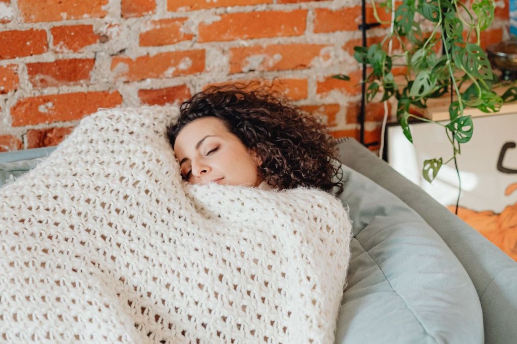 Femme qui se repose sur un canapé, emmitouflée dans une couverture en maille