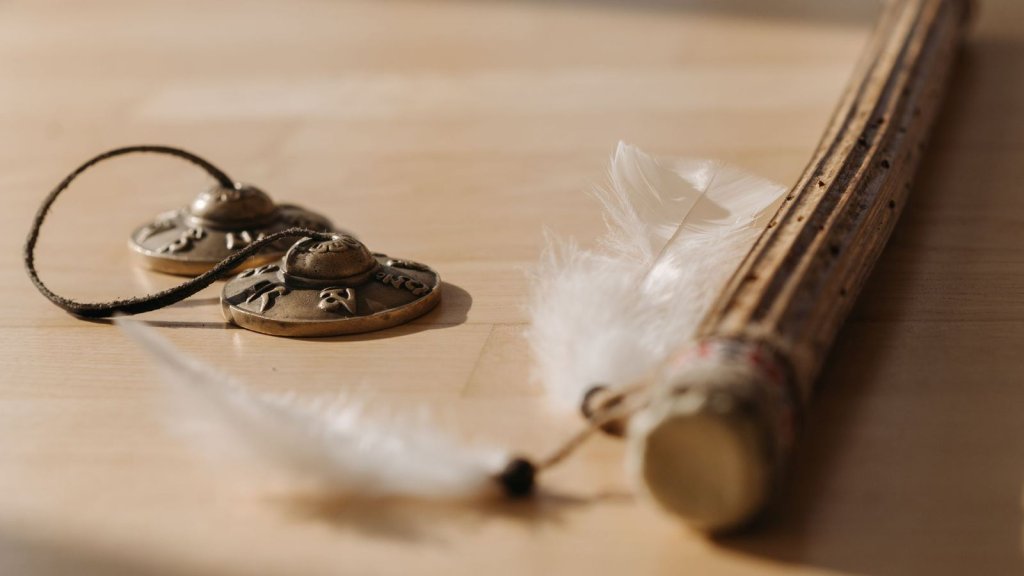 Cymbales tibétaines, plume blanche et bâton de bois posés sur une table claire