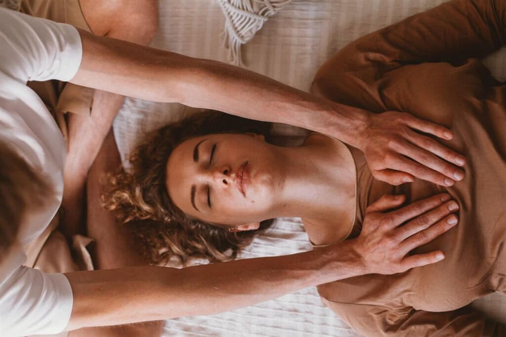 Femme allongée et habillée, les yeux fermés, recevant un soin énergétique par imposition des mains