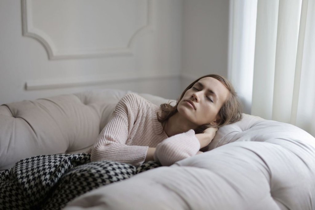 Femme habillée allongée sur un canapé, les yeux fermés, détendue sous un plaid